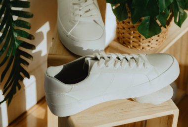 Güzel beyaz klasik bir spor ayakkabı, tahta vitrinlerde doğal bir taşın üzerinde duruyor. Güneşli bir günde, evin yanındaki mağazanın kapısının yanındaki hasır tencerede bir çiçek var. Üst taraf manzarası tarlanın derinliği ile çok yakın. Kadın ayakkabıları.