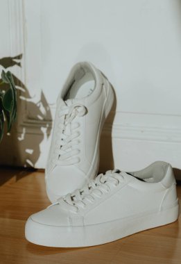 Yüksek tabanlı ve dantelli bir çift güzel beyaz spor ayakkabı güneşli bir günde bir ev mağazasının kapısındaki hasır bir saksıda lamine bir çiçekle birlikte, tarlanın derinliğiyle çok yakın bir şekilde duruyor. Kadın ayakkabıları.