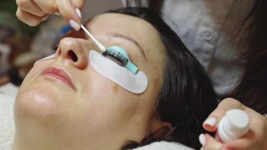 Beyaz tenli tanınmayan genç bir kozmetik uzmanının elleri, sol gözünün kirpiklerini pamuklu çubukla temizliyor, bir müşterinin kozmetoloji masasında uzanan bir müşterisinin, bir güzellik salonunun yan görünüşü çok yakın. Konsept