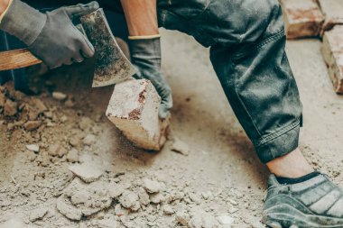 İş kıyafetleri ve eldivenleriyle tanınmayan genç beyaz bir adamın portresi, balta kullanarak toprak ve eski çimentodan tuğlaları temizliyor, küçük bir sandalyede oturuyor, bacakları aralıklı bir şekilde yenilenmekte olan bir odada, yan görüş çok yakın. İnşaat kavramı
