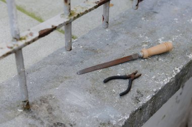 Eski bir pense ve bir dosya bir bahar günü arka bahçedeki beton pencere pervazında duruyor. Üst taraf manzaralı, orta ölçekli. Konsept inşaat araçları, ilkbahar çalışmaları.