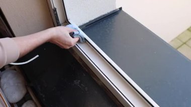 Tanınamayan genç bir beyaz adam plastik bir pencere çerçevesinin içini ikinci kattaki bir odada duran mavi bir mikrofiber bez ile yıkıyor. Yan manzara yavaş çekimde. Pencere çerçevelerinin onarımı ve yalıtımı kavramı, ilkbahar