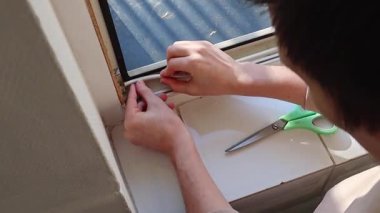 Beyaz tenli esmer adam, kendi kendine yapışkan beyaz kauçuk profilini pencere çerçevelerine yapıştırıyor. Yan tarafından yavaş çekimle yakın çekim. Pencere çerçevelerinin onarımı ve yalıtımı kavramı, ilkbahar çalışmaları.