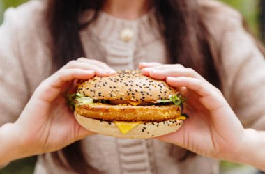 Tanımlanamayan beyaz bir kadın elinde tavuk pirzolası ve iki eliyle salata tutan taze bir burgerle yaz günü kafede terasta oturuyor. Zaman, fast food demektir..
