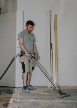 İş kıyafetleri içindeki beyaz tenli genç adam inşaat süpürgesiyle yerleri süpürüyor. Tadilatın sürdüğü eski bir evde, aşağıdan seçici bir odaklanma ile yakın plan görüntüsü var. İnşaat konsepti..