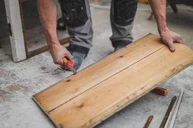 Kafkas görünümlü tanınmayan genç bir marangoz sökülmüş eski bir ahşap kapının tahtasından çivileri söküyor, tamir çalışmalarının yapıldığı bir odada duruyor, yakından bakıyor. İnşaat işi, marangoz.