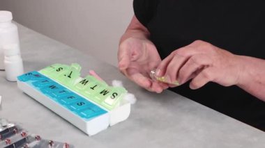 Tanınmayan üst düzey bir kadın cımbızla şişeden pamuk alır ve sarı hapları bir depo konteynırının hücresine koyar, gündüz vakti bir masada oturur, yan görüntüyü yavaş çeker.İlaçları alırken zaman kavramı