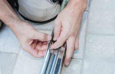 Yazın metal bir ahırın çatısını elle vidalayan, tanınmayacak kadar olgun bir beyaz adam, çok yakın plan. Metal ambarın teknoloji ve zaman ekip çalışması kullanılarak birleştirilmesi.