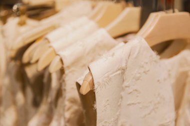 Alışveriş merkezindeki bir mağazadaki ahşap askılarda asılı bej renkli püsküllü elbiselerin güzel manzarası, seçici bir odak ile yan manzara. Konsept alışveriş zamanı, kadın kıyafetleri.
