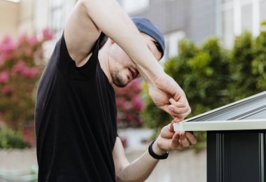 Siyah tişörtlü beyaz adam manuel olarak cıvataları sıkıyor. Arka bahçedeki metal barakanın çatısına kapak takıyor. Teknoloji kullanarak metal dökme konsepti.