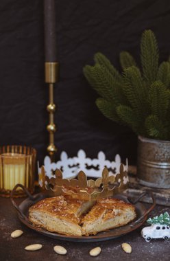 Güzel bir retro metal plaka, üç lezzetli kraliyet galeti ile doldurulmuş koyu bir masa, altın bir taç, dağınık badem, bir oyuncak, bir mum ve ladin dalları, bir kenar görüş yakın. Konsept tatil zamanı, yemek zamanı.