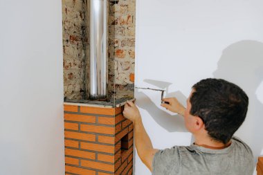 Beyaz tenli genç bir adam taze çimento harcı döşeyen bir mala ve ince bir ahşap bir katman kullanarak şömine bacasında temiz tuğla yapıyor, üst tarafı seçici bir odak ile yakın görüyor. Temiz tuğla işi konsepti, aile evi tadilatı.