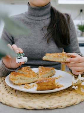 Mutfak masasında oturan, elinde bir parça kraliyet bisküvisi ve oyuncak bir hediyeyle çok yakından çekilmiş beyaz bir kızın dikey portresi. Konsept: tatil zamanı, kraliyet bisküvisi yeme zamanı.
