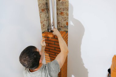 Taze çimento harcı döşeyen genç beyaz bir adam, çekiçle tuğlaya vuruyor, şöminenin bacasında temiz bir tuğla yapıyor, seçici bir odak ile yukarıdan aşağıya yakın bir bakış. Temiz tuğla işi konsepti, aile evi tadilatı.