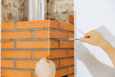 Tanınmayan genç bir beyaz adam, şömine bacasındaki tuğlalar arasında gün boyunca sandalyede dururken dar ve uzun bir spatula kullanarak aşırı taze çimento harcı temizliyor. Temiz