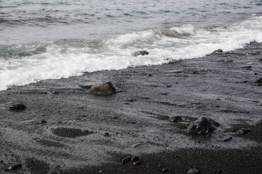 Aşağıdan, Tenerife 'de bir sonbahar günü, siyah bir volkanik çakıl taşları ve kaldırım taşlarından oluşan kumsalda sakin dalgaların güzel atmosferik görüntüsü. Doğanın arka planlarını ve duvar kağıtlarını kavra.