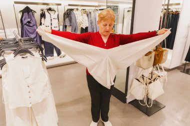 Güzel bir beyaz kadın portresi, kırmızı bluzlu, pantolonunun uzunluğunu ölçen, bahar günü dükkanda duran, yan görünümü yakından gören. Konsept zaman alışverişi, emeklilik yaşam tarzı, son sınıf öğrencileri.