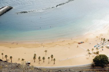 Palmiye ağaçları ve Atlantik Okyanusu 'nda bir sonbahar günü, yakından görünen bir adada gezinen tanınmayan insanlarla dolu kumlu bir sahil manzarası. Konsept: seyahat zamanı, sonbahar zamanı.