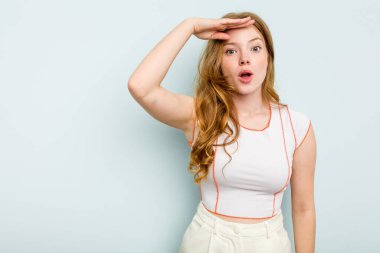 Kafkasyalı genç bir kadın mavi arka planda izole edilmiş, uzaklara bakıyor ve elini alnına koyuyor..