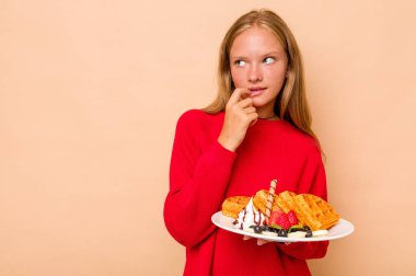 Beyaz tenli küçük bir kız, elinde bej arka planda izole edilmiş waffle 'lar tutuyor. Bir şeyin fotokopi odasına baktığını düşünüyor..