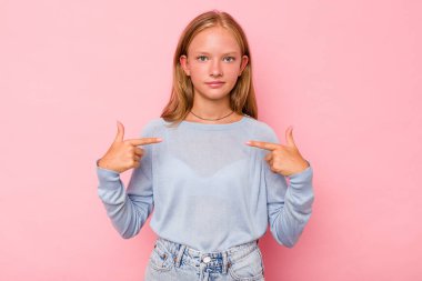 Pembe arka planda izole edilmiş beyaz bir kız tişört fotokopisini elle gösteriyor, gururlu ve kendinden emin.