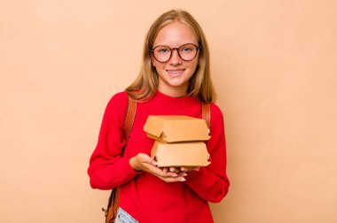 Bej arka planda izole edilmiş hamburgerleri tutan küçük beyaz kız gülüyor ve eğleniyor..