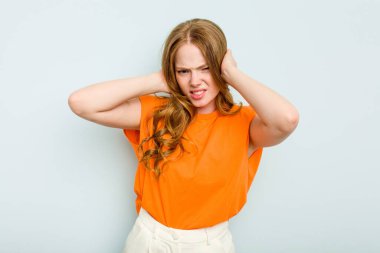 Mavi arka planda izole edilmiş genç beyaz kadın kulaklarını elleriyle kapatıyor..