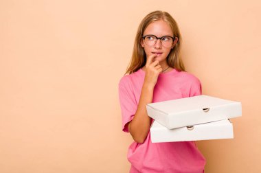 Elinde pizza tutan beyaz bir kız bej arka planda izole edilmiş. Bir şeyin fotokopi odasına baktığını düşünüyor..