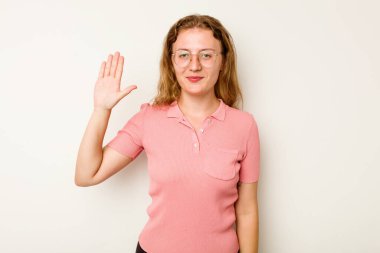 Beyaz arka planda izole edilmiş genç beyaz kadın gülümseyerek beş numarayı parmaklarıyla gösteriyor..