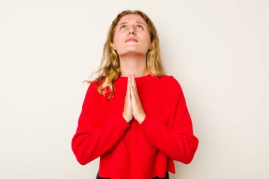 Beyaz arka planda izole edilmiş genç beyaz bir kadın el ele dua ederken, kendine güveniyor..