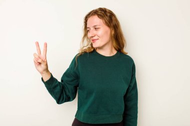 Beyaz arka planda izole edilmiş genç beyaz kadın neşeli ve kaygısız parmakları olan bir barış sembolü gösteriyor..