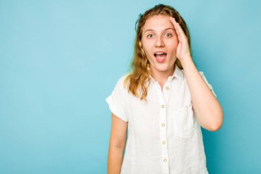Mavi arka planda izole edilmiş genç beyaz kadın yüksek sesle bağırıyor, gözlerini açık ve ellerini gergin tutuyor..