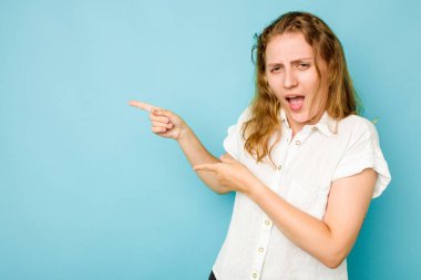 Mavi arka planda izole edilmiş genç beyaz kadın işaret parmaklarıyla fotokopi alanını işaret ederek heyecan ve arzusunu ifade ediyor..