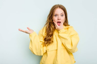 Mavi arka planda izole edilmiş beyaz bir kadın avuç içinde fotokopi alanı tutuyor, el üstünde tutuyor. Şaşırmış ve mutlu..