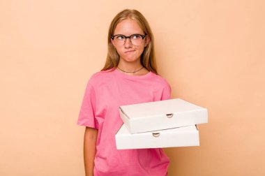 Elinde bej arka planda izole edilmiş pizza tutan küçük beyaz kız kafası karışmış, şüpheli ve güvensiz hissediyor..