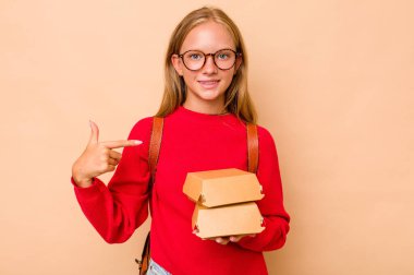 Elinde hamburgerlerle gezen küçük beyaz kız bej arka planda oturan kişi gömlek fotokopi alanını işaret ediyor, gururlu ve kendinden emin.