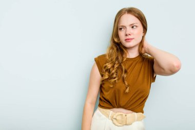 Kafkasyalı genç bir kadın mavi arka planda izole edilmiş kafasının arkasına dokunuyor, düşünüyor ve bir seçim yapıyor..