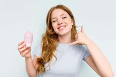 Mavi arka planda deodorant tutan beyaz bir kadın cep telefonu hareketini parmaklarıyla gösteriyor..