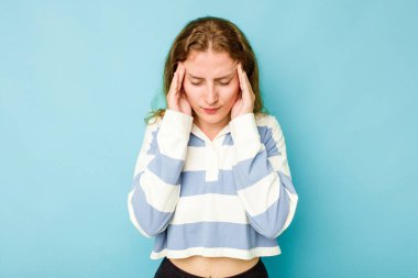 Mavi arka planda izole edilmiş genç beyaz kadın şakaklara dokunuyor ve baş ağrısı çekiyor..