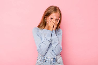 Pembe arka planda izole edilmiş beyaz bir kız kameraya parmaklarıyla göz kırpıyor, yüzünü kapatmaktan utanıyor..