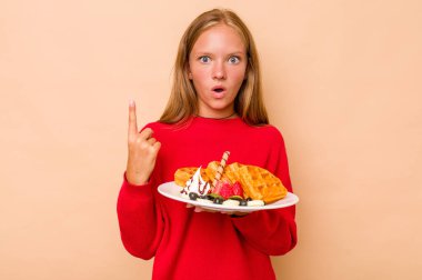 Elinde bej arka planda izole edilmiş waffle tutan beyaz bir kız. Harika bir fikri var, yaratıcılık kavramı..
