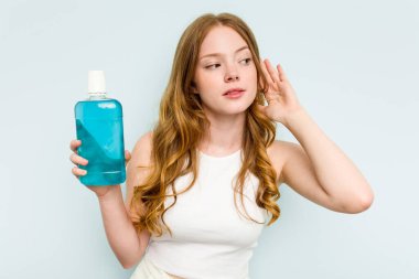 Elinde gargara tutan beyaz bir kadın mavi arka planda izole edilmiş bir şekilde bir dedikoduyu dinlemeye çalışıyor..