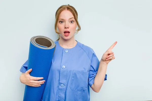 Young Caucasian Physiotherapist Holding Mat Isolated Blue Background Pointing Side — Stock Photo, Image