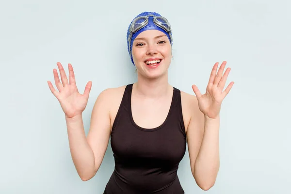 年轻的高加索游泳女子 身披蓝色背景 带着惊喜 兴奋地举起双手 — 图库照片