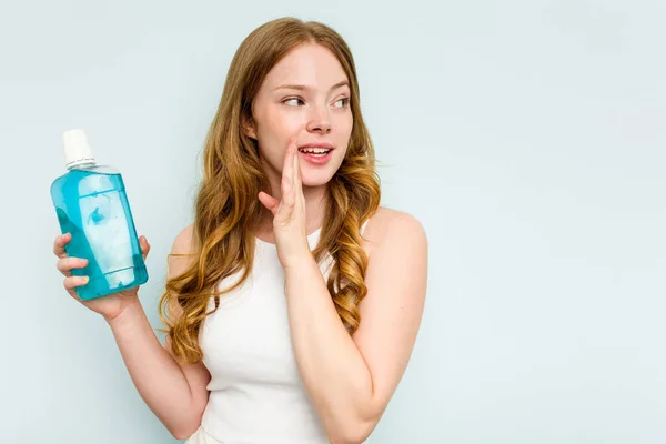 stock image Young caucasian woman holding a mouthwash isolated on blue background is saying a secret hot braking news and looking aside