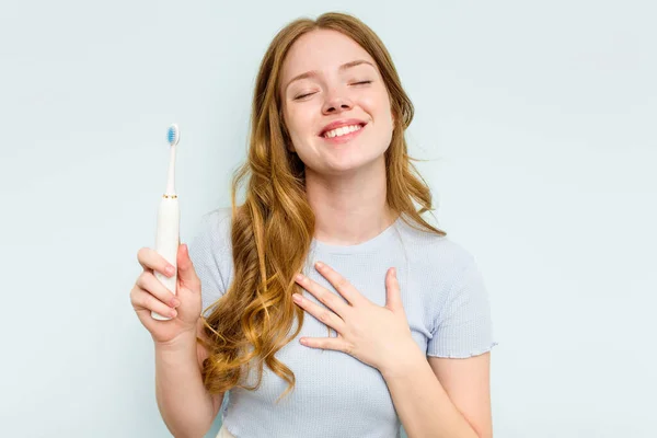 若いです白人女性を保持電気歯ブラシ隔離上の青の背景笑アウト大声で手を保つ胸 — ストック写真