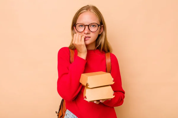 小高加索女学生拿着被米色背景隔离的汉堡包 咬着指甲 紧张而焦虑 — 图库照片