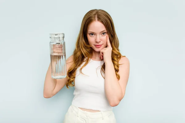 Mladá Běloška Drží Sklenici Vody Izolovanou Modrém Pozadí Ukazující Prstem — Stock fotografie