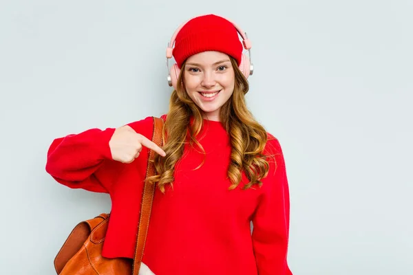 stock image Young student woman wearing headphones isolated on blue background person pointing by hand to a shirt copy space, proud and confident