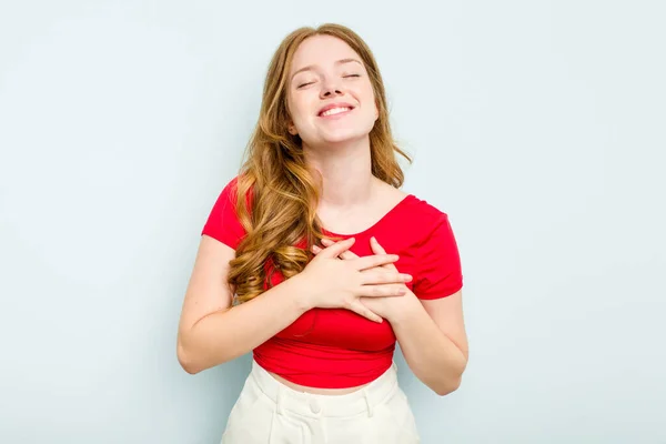 青い背景に孤立した若い白人女性が手を心に留め笑い 幸福の概念 — ストック写真